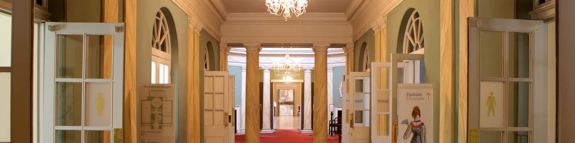 A grand hallway with a red carpet, chandeliers, and doors leading to various rooms including a fashion museum and a shop.