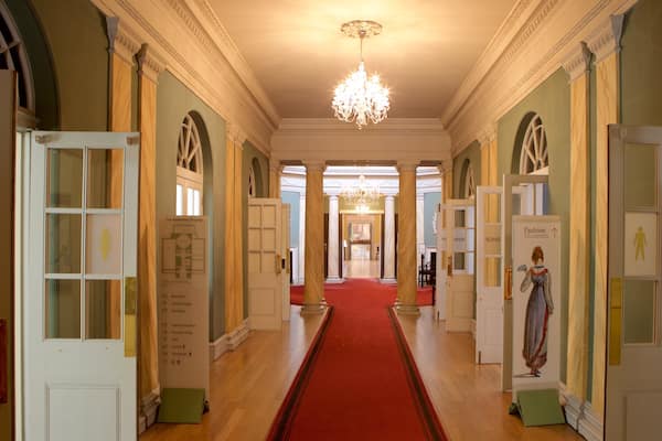 Un vaste hall d’entrée avec un tapis rouge, des lustres et des portes donnant accès à différentes pièces, notamment un musée de la mode et une boutique.