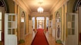 A grand hallway with a red carpet, chandeliers, and doors leading to various rooms including a fashion museum and a shop.