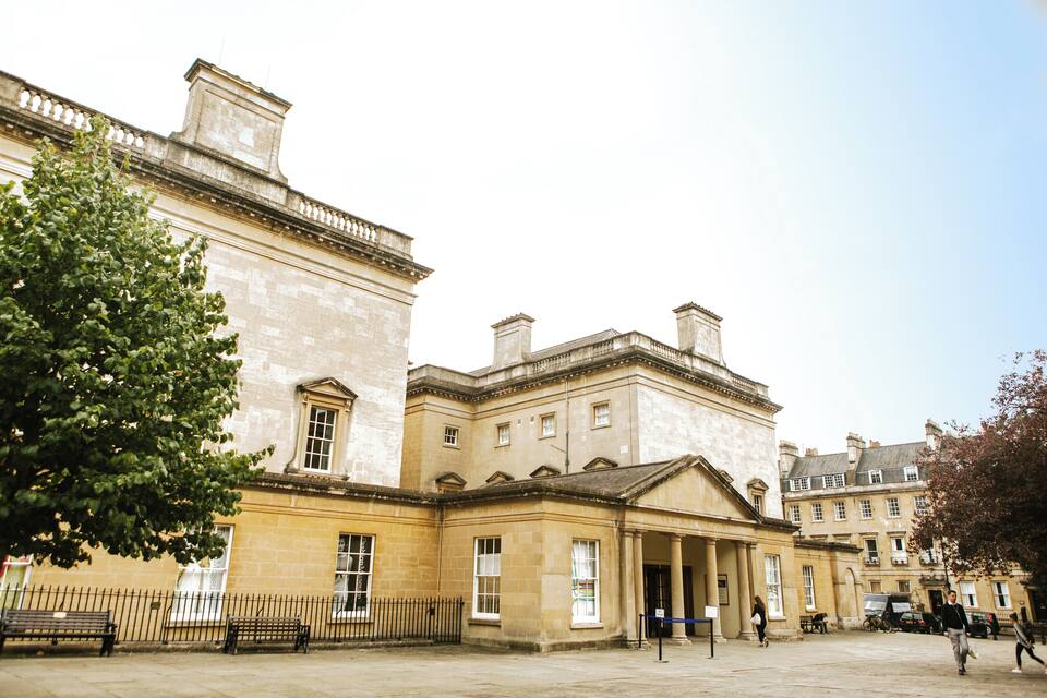 A historic building with classical architecture, a paved courtyard, and a tree.