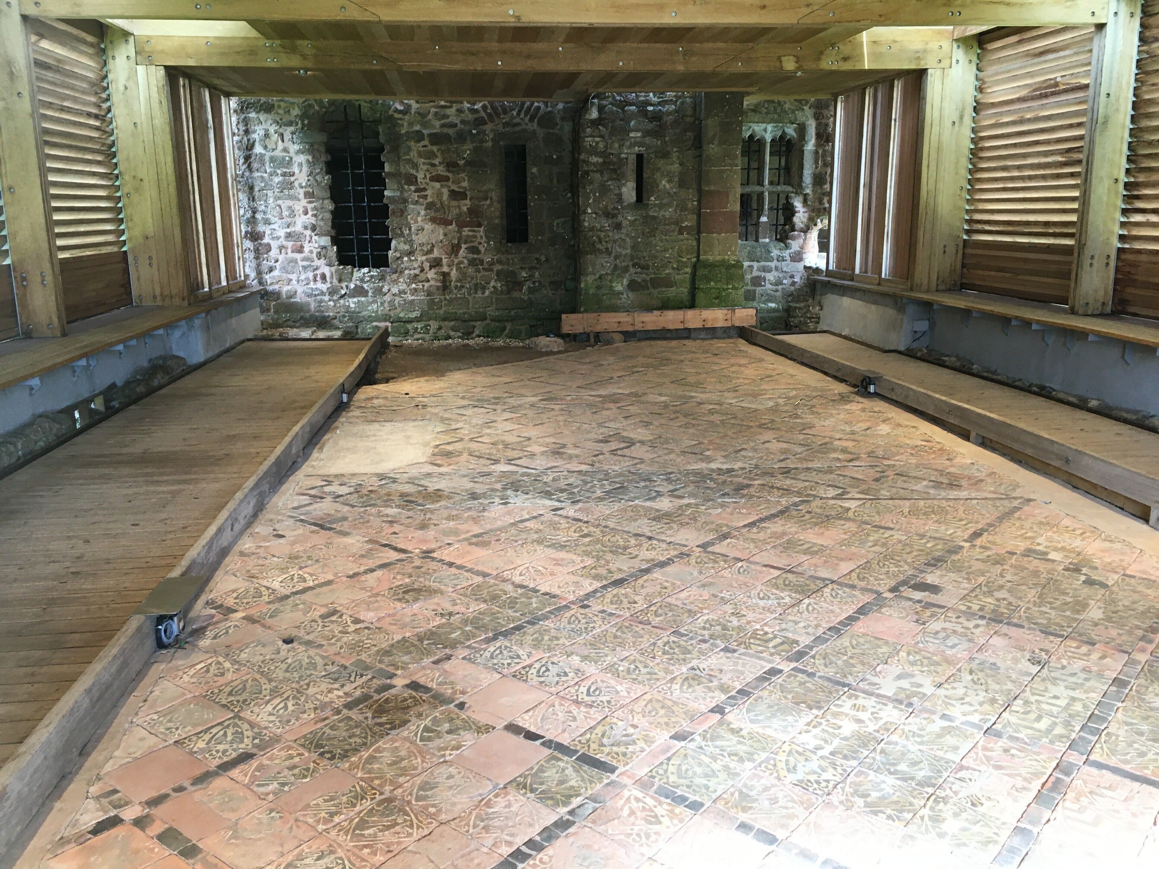 A room with patterned tiled flooring, wooden beams, and stone walls.
