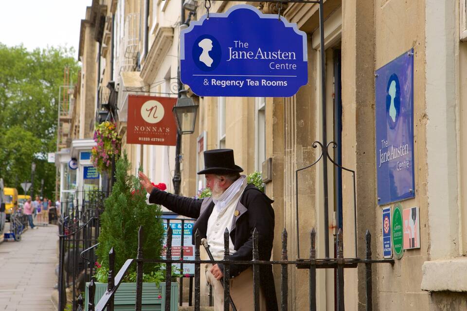 Et gadesceneri med en mand, der peger på et skilt for The Jane Austen Centre & Regency Tea Rooms.