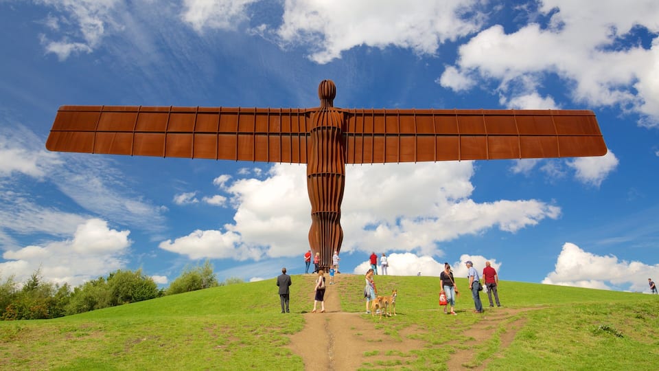A large metal sculpture with outstretched wings on a grassy hill under a blue sky with clouds.