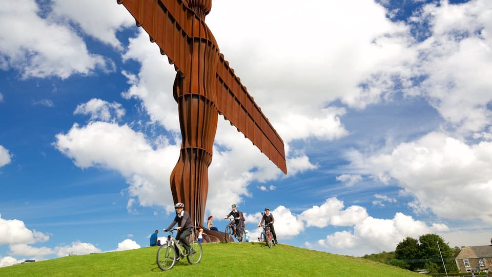 A large metal sculpture on a grassy hill with cyclists.