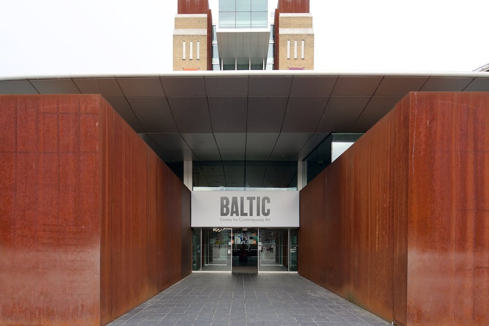A entrada do Baltic Centre for Contemporary Art, com um design moderno que apresenta grandes painéis de madeira e fachada de vidro.