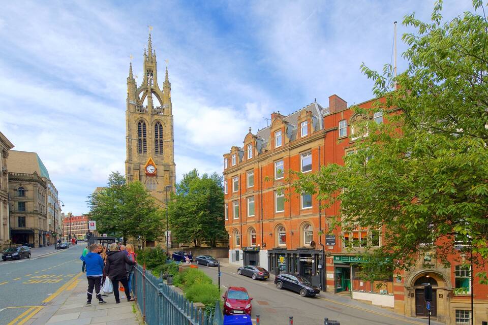 A historic church with a tall spire, a red brick building, and a street with pedestrians and cars.