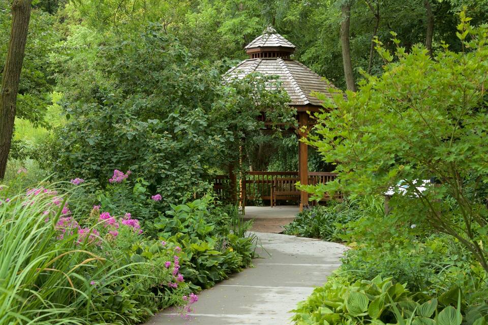 A gazebo surrounded by lush greenery and flowering plants.