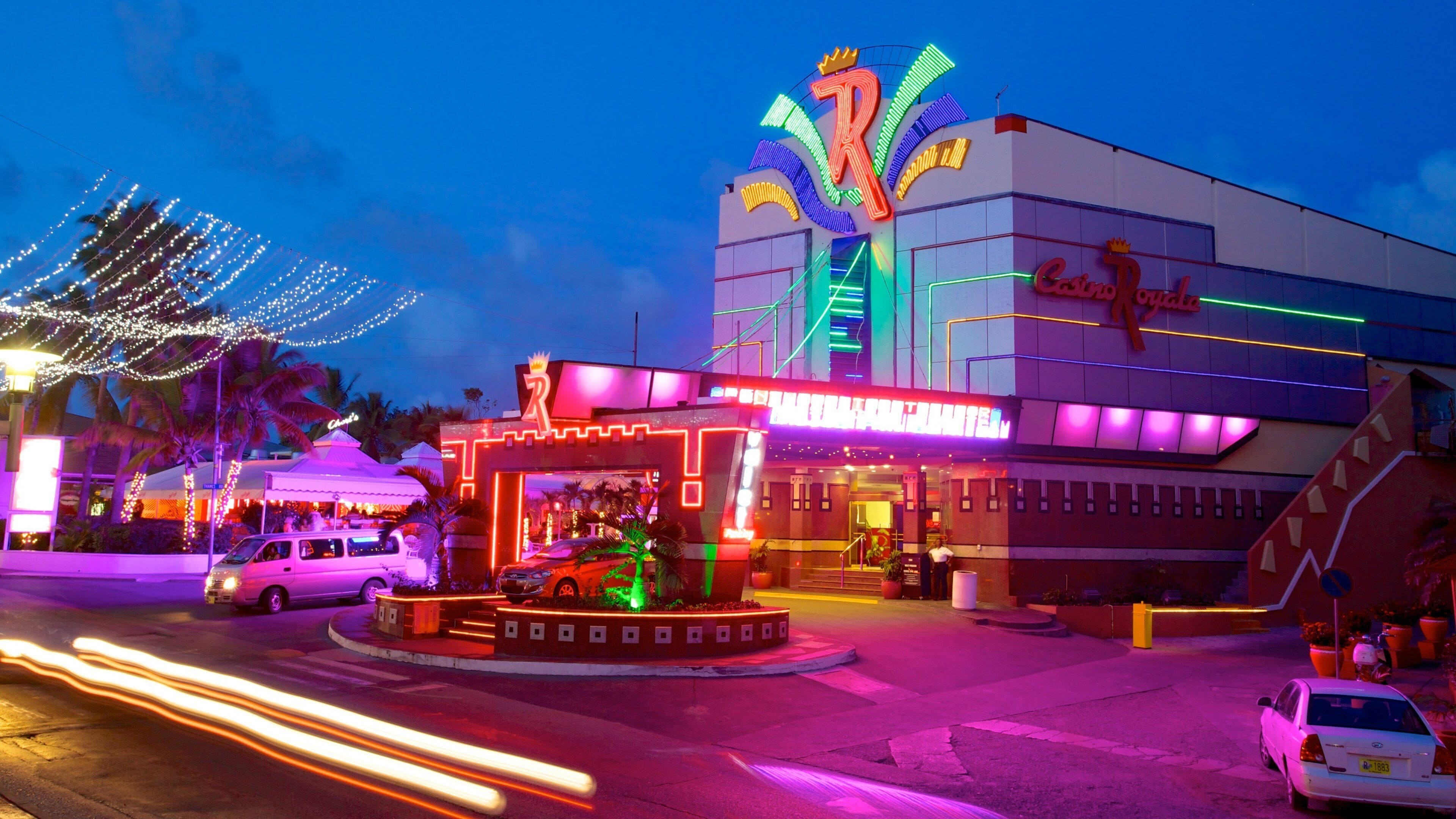 Un casino muy iluminado con letreros de neón y una palmera en primer plano.
