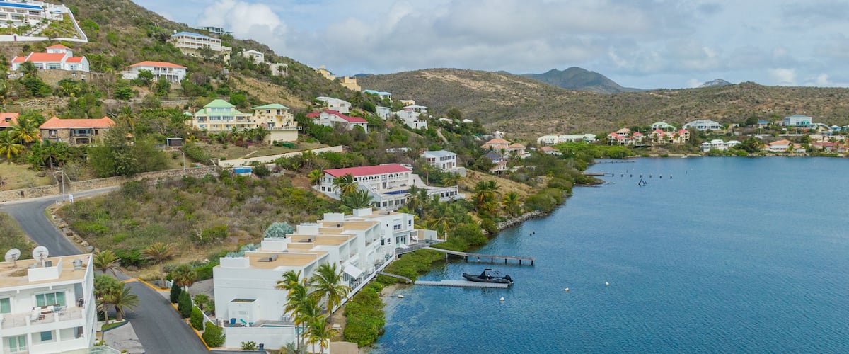 A coastal town with buildings along the waterfront, a dock, and a clear blue sea.