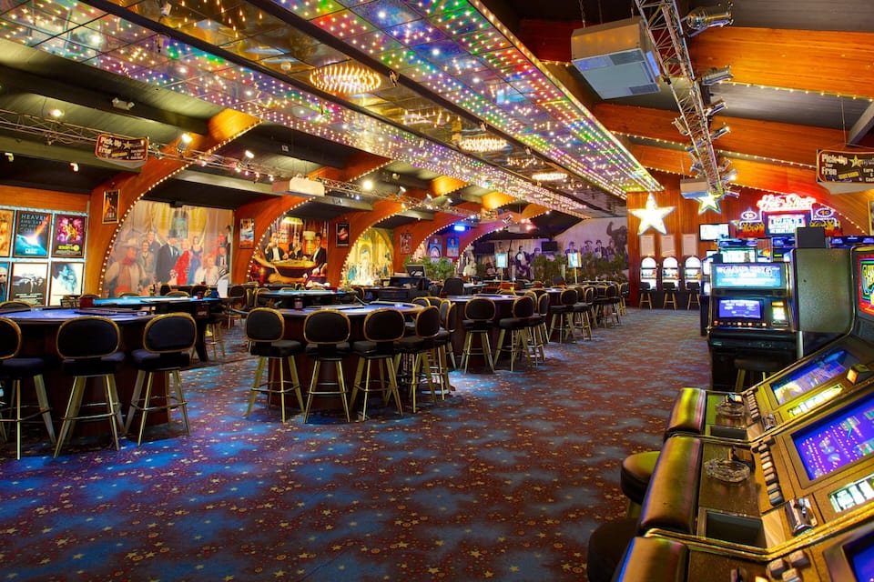 Interior de casino amb màquines escurabutxinador, taules de blackjack i il·luminació colorida.