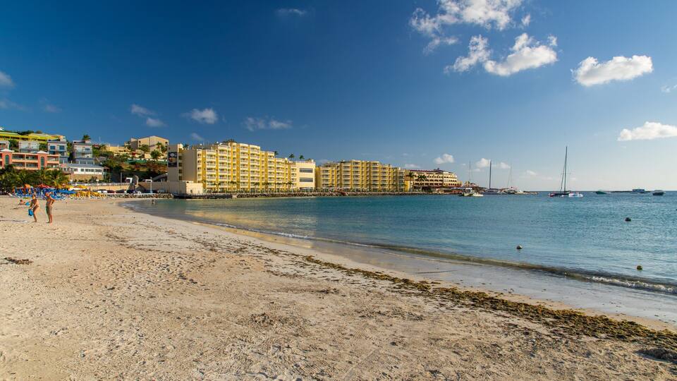 A beach with a sandy shore, a row of yellow buildings, and sailboats in the water.
