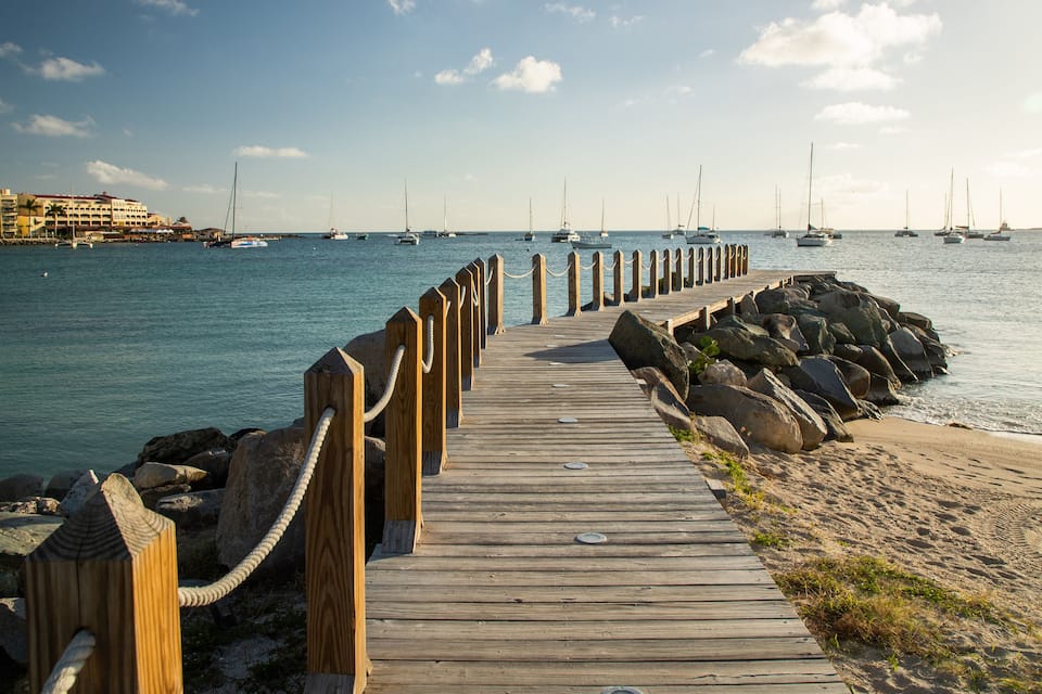 A wooden pier extending into calm waters with sailboats anchored nearby.