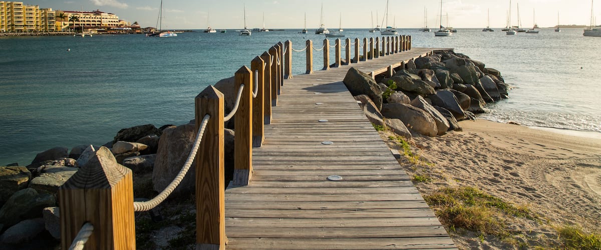 A wooden pier extending into calm waters with sailboats anchored nearby.