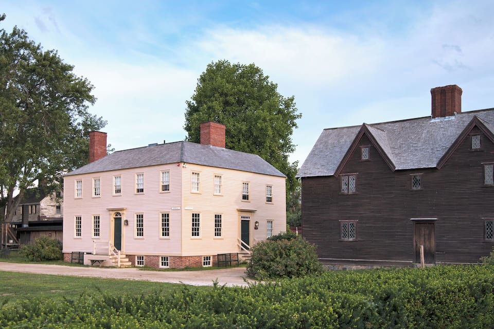 A historic two-story building with a light-colored facade and a dark wooden structure adjacent to it.