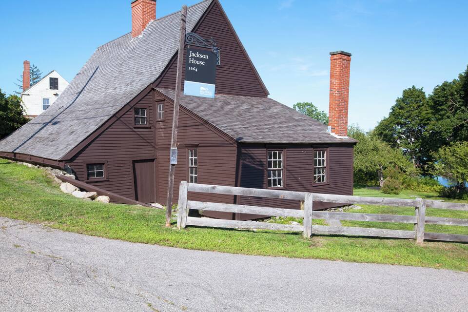 Una casa histórica con un letrero que dice "Jackson House 1664" y una cerca de madera al frente.