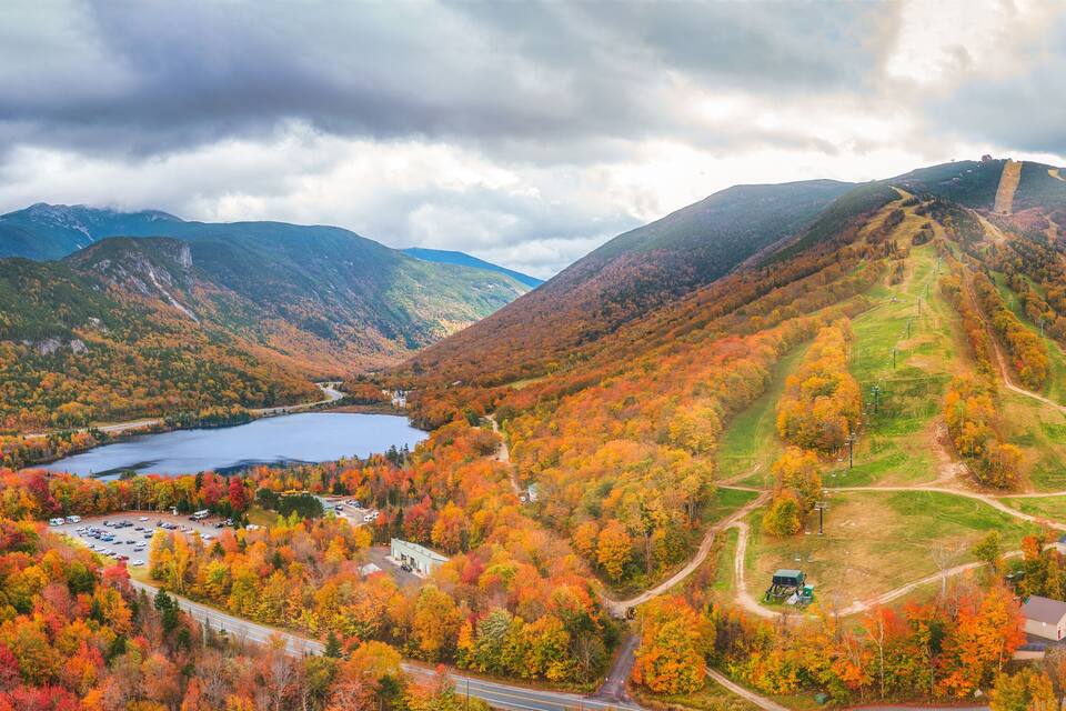 A mountainous landscape with autumn foliage, a lake, and a small settlement with buildings and roads.