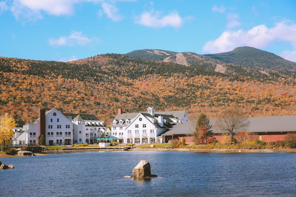 A lakeside town with white buildings, autumn foliage, and a mountain in the background.