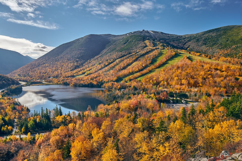 A mountainous landscape with a lake surrounded by autumn-colored trees.