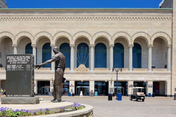 A statue of a man in front of a building with arched windows and columns.
