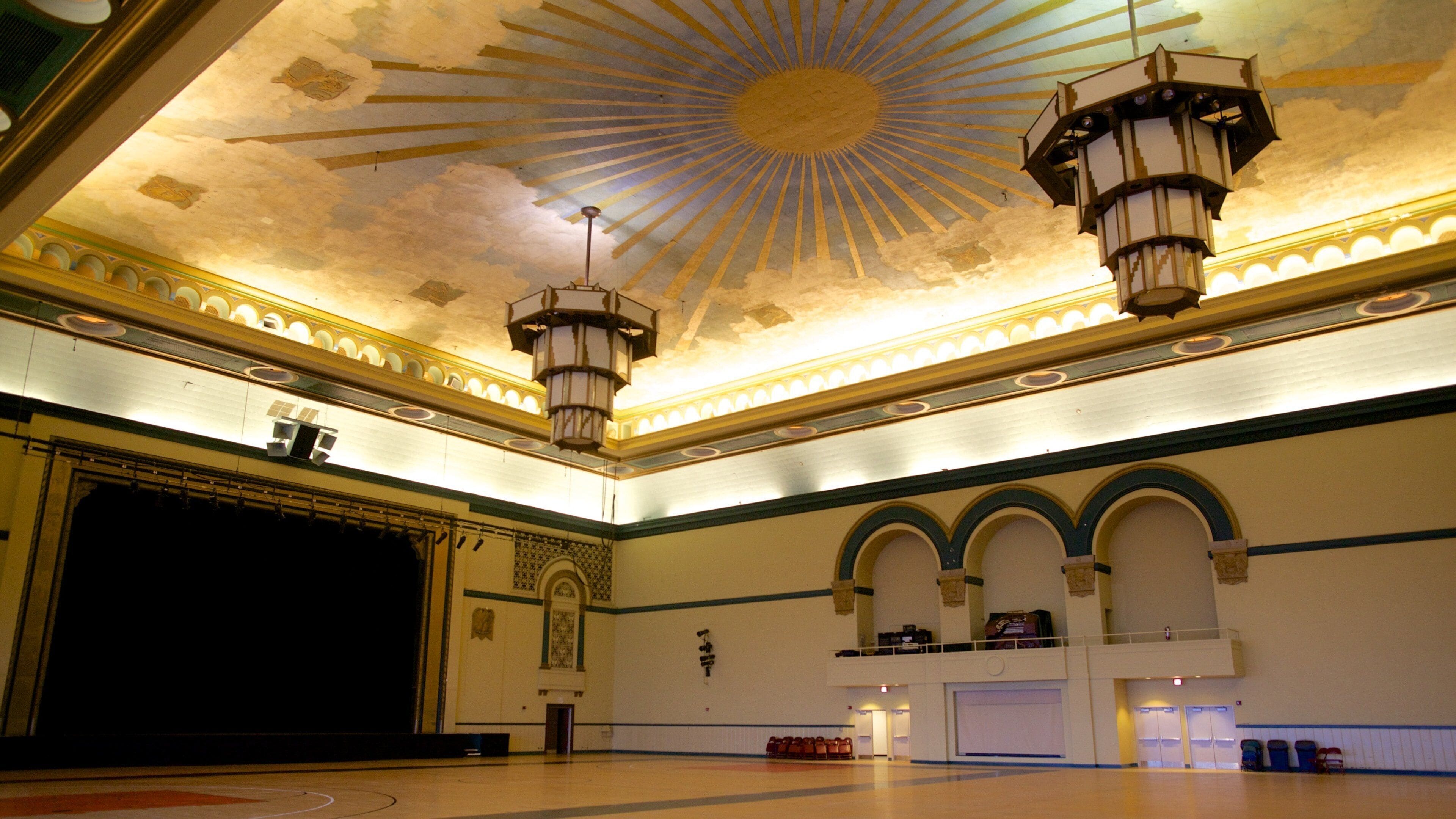 Un salón imponente con un techo en forma de sol, columnas ornamentadas y un escenario.