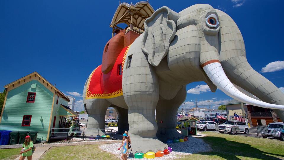 A large elephant sculpture with a red saddle and a house in the background.