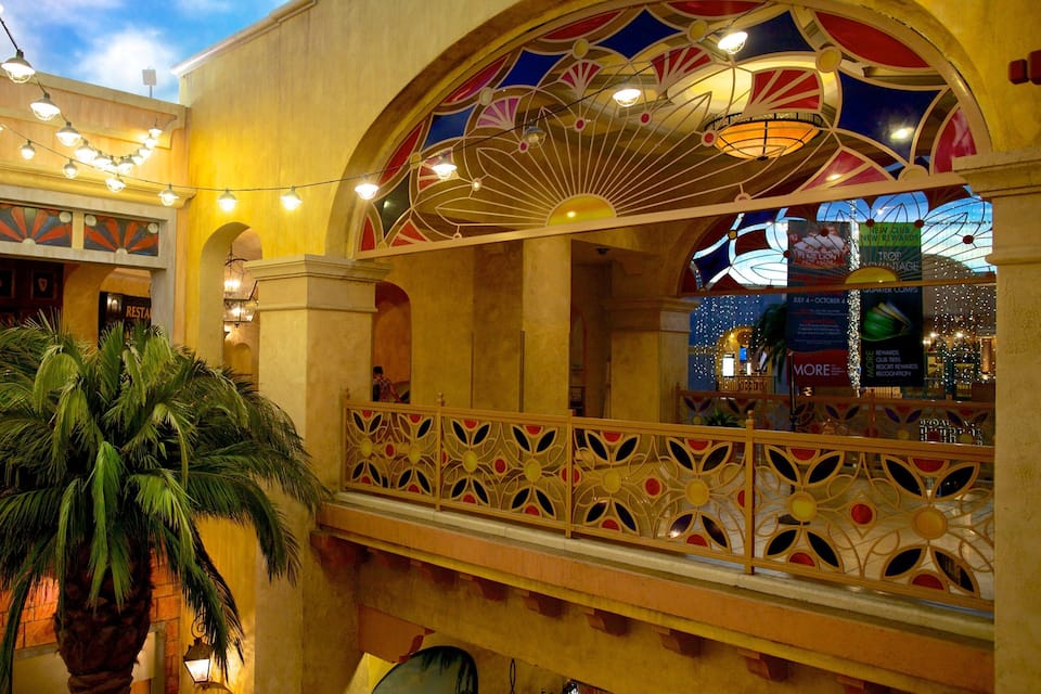 A brightly lit atrium with string lights, a palm tree, and a decorative balcony railing.