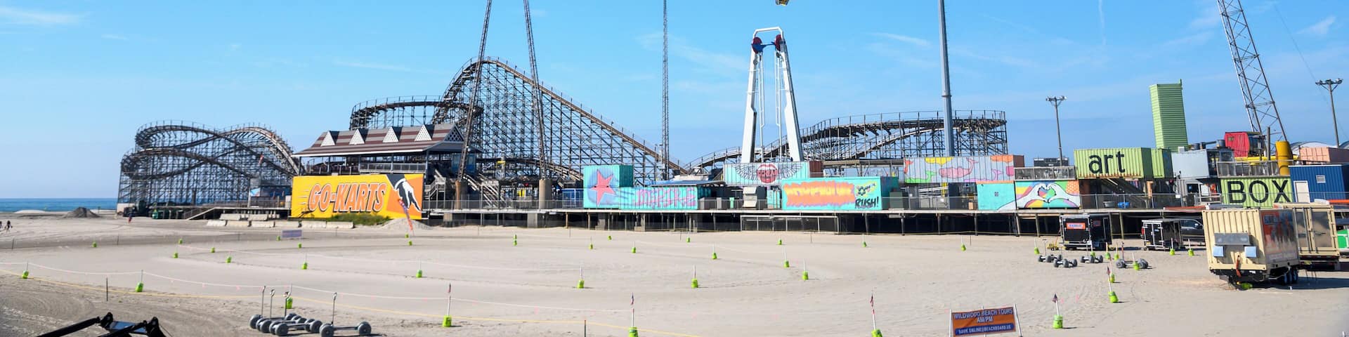 A roller coaster under construction with scaffolding and cranes, surrounded by a sandy area with construction cones.