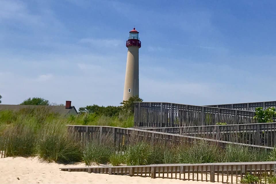 Un phare se dresse sur une plage de sable, et une promenade en bois mène jusqu’à sa base.