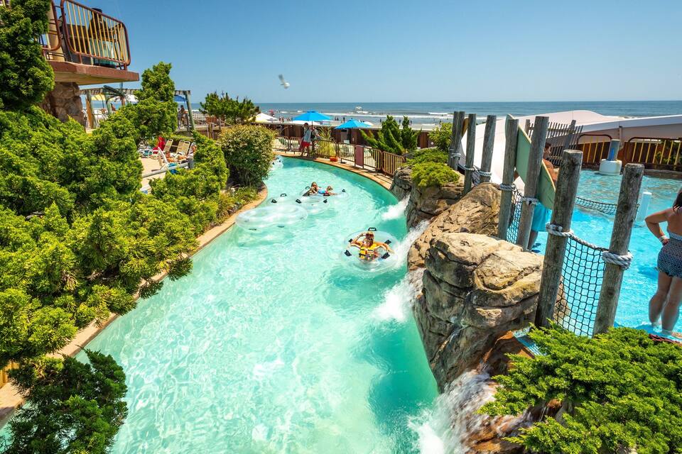 Parque acuático con río lento, cascada y zona de piscina rodeada de vegetación.