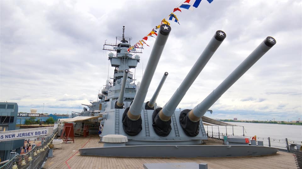 A naval ship with multiple large guns, a dock area, and a sign reading "USS NEW JERSEY BB-62".