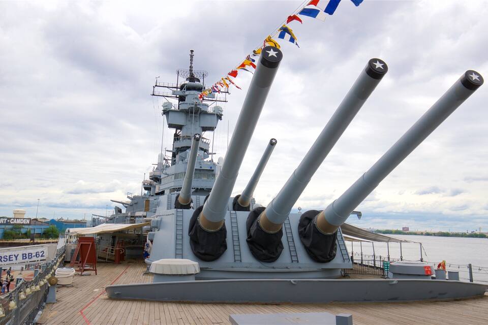 A naval ship with multiple large guns, a dock area, and a sign reading "USS NEW JERSEY BB-62".