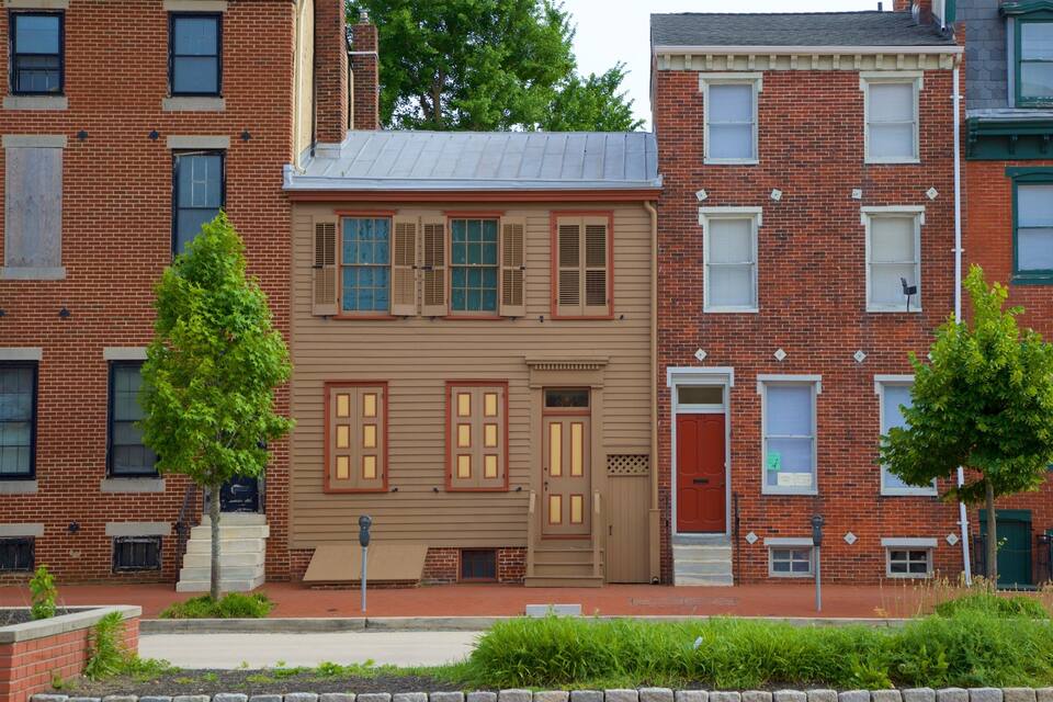 A row of red brick townhouses with green window frames, a beige building with brown shutters, and a red door.