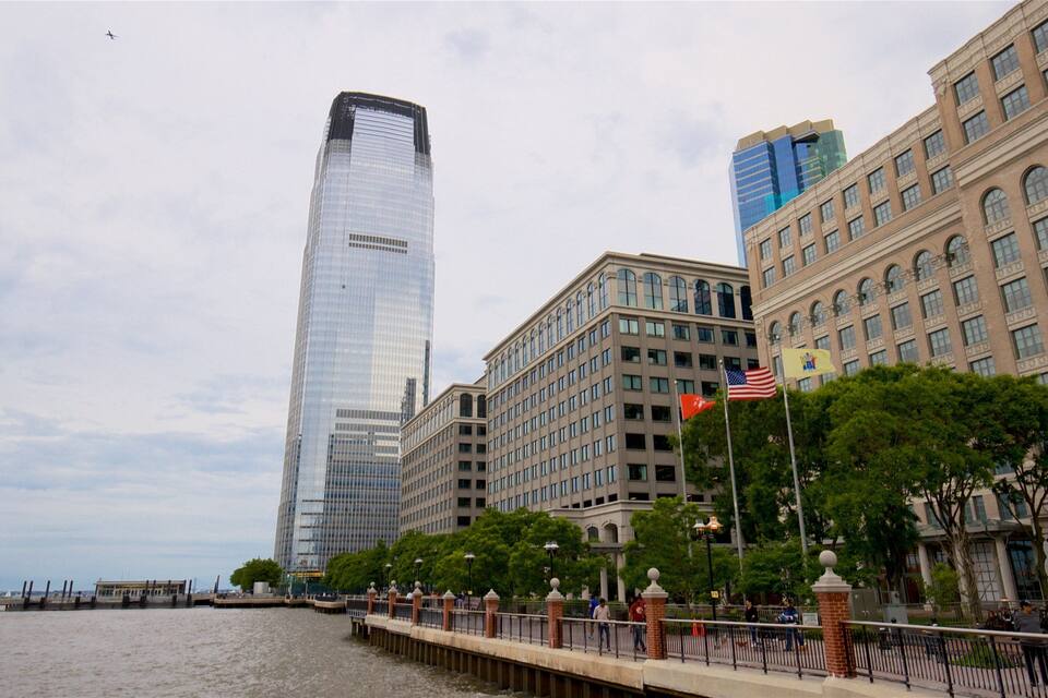 A waterfront cityscape with modern skyscrapers, including a prominent glass building, and a historic building with flags.