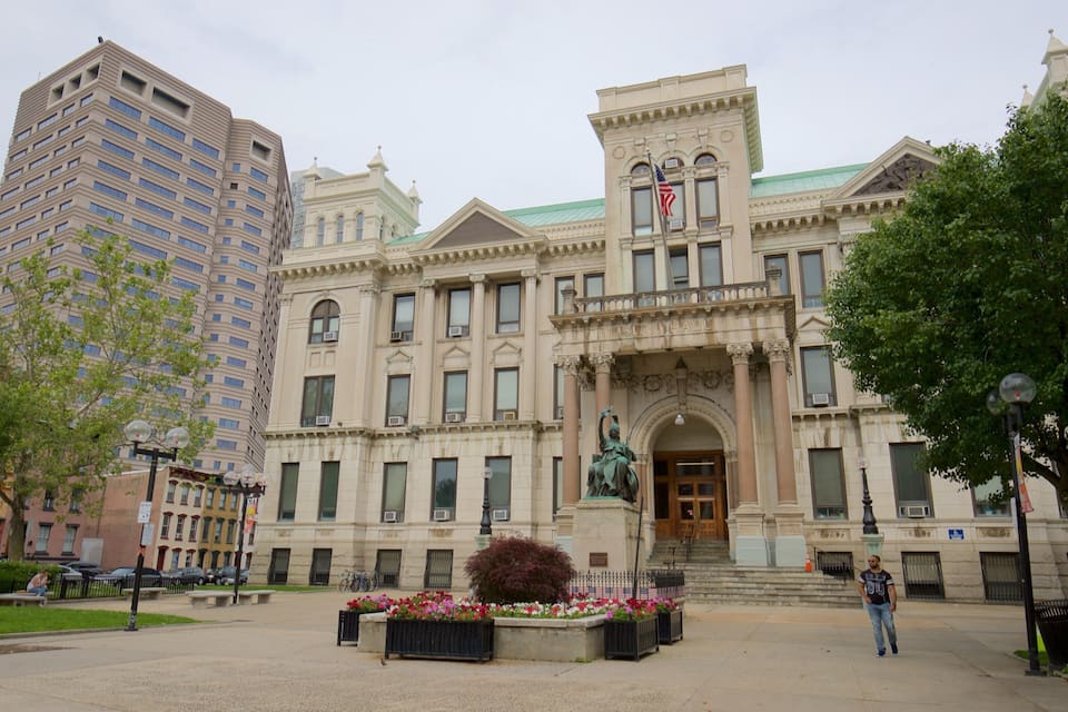 A historic building with classical architecture, a statue in front, and a modern high-rise building nearby.