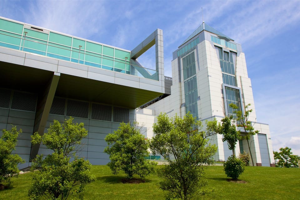 A modern building with glass and metal architecture, surrounded by green grass and trees.