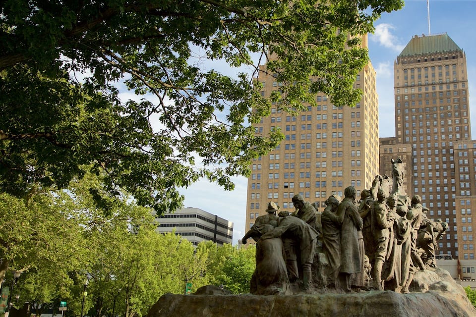 Estátua de soldados em um parque, com edifícios altos ao fundo.