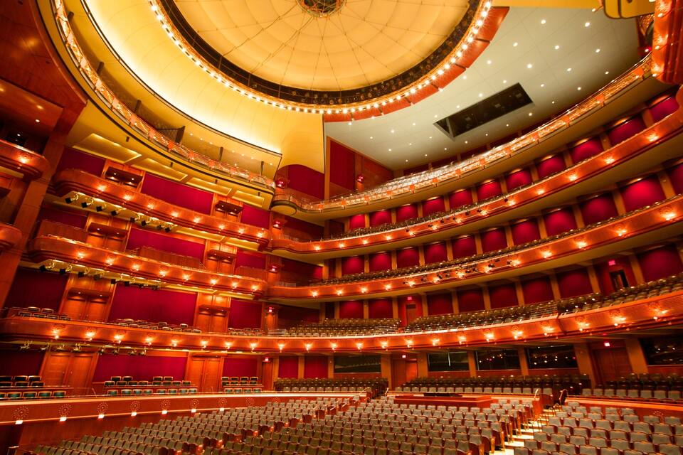 Um grande auditório com vários níveis, assentos vermelhos e um palco circular.