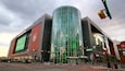 Un bâtiment moderne doté d’une façade en verre incurvée, d’un logo bien visible sur le côté et d’un panneau de signalisation indiquant la rue Mulberry.