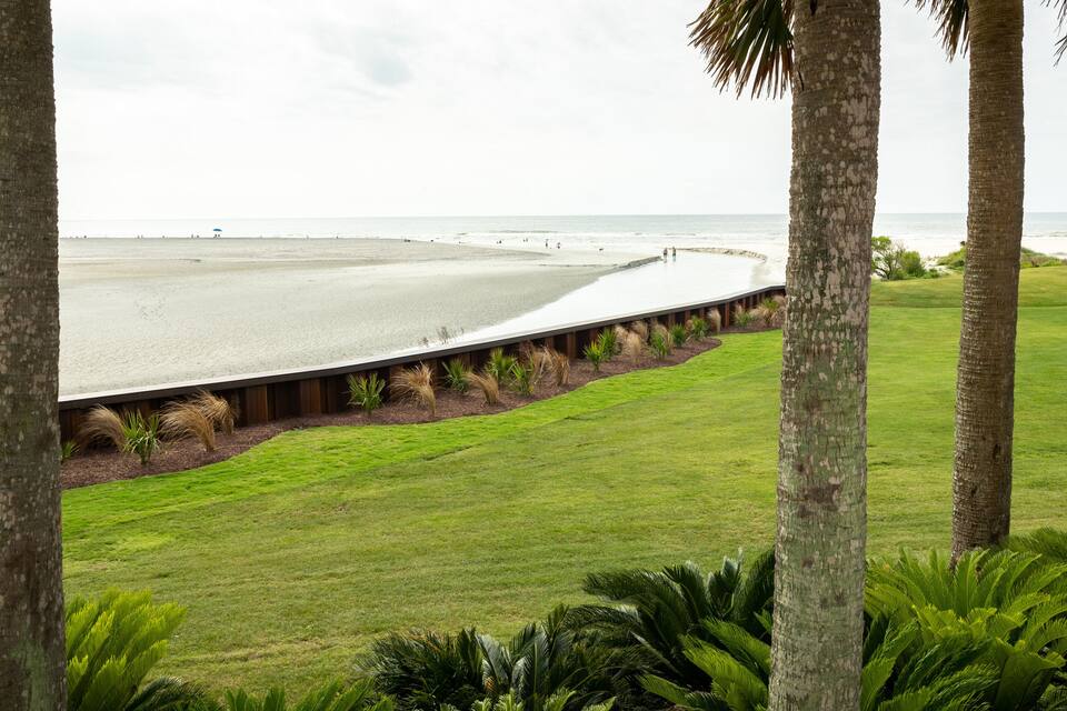 A beach with a concrete walkway, palm trees, and grassy areas.