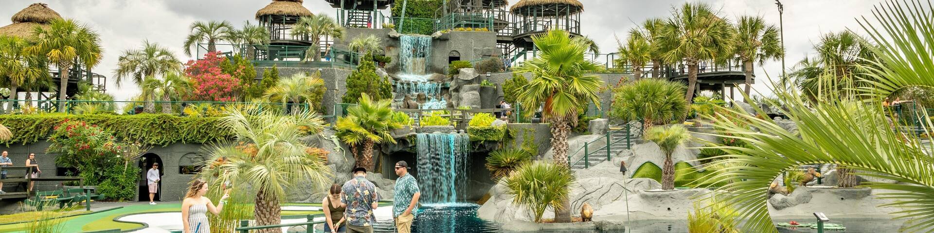 A tropical resort with a large pool, palm trees, and a waterfall.