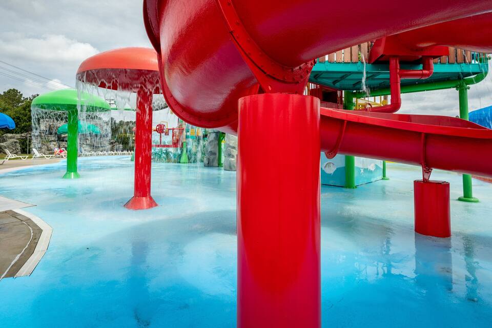 Um parque aquático com um tobogã aquático vermelho, atrações com água verde e azul, e uma área de piscina.