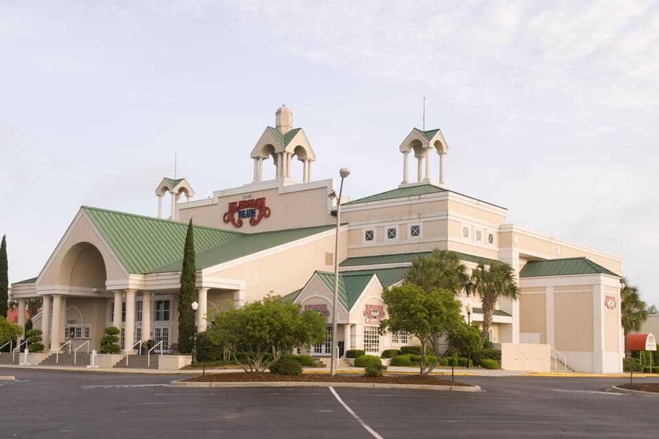 A large building with a green roof and multiple towers, featuring a prominent sign with a red and white emblem.