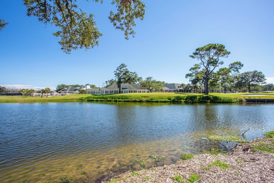 A calm lake with clear water, surrounded by green grass and trees.
