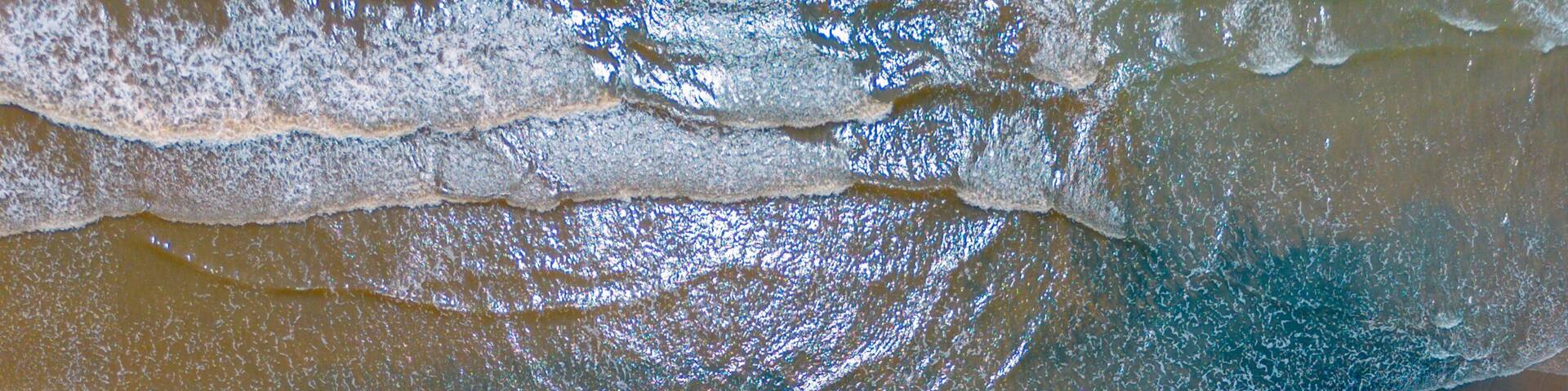 Aerial view from drone in bengkulu, indonesia showing turquoise indian waters, sandy beaches, small boats, and lush tropical hills.