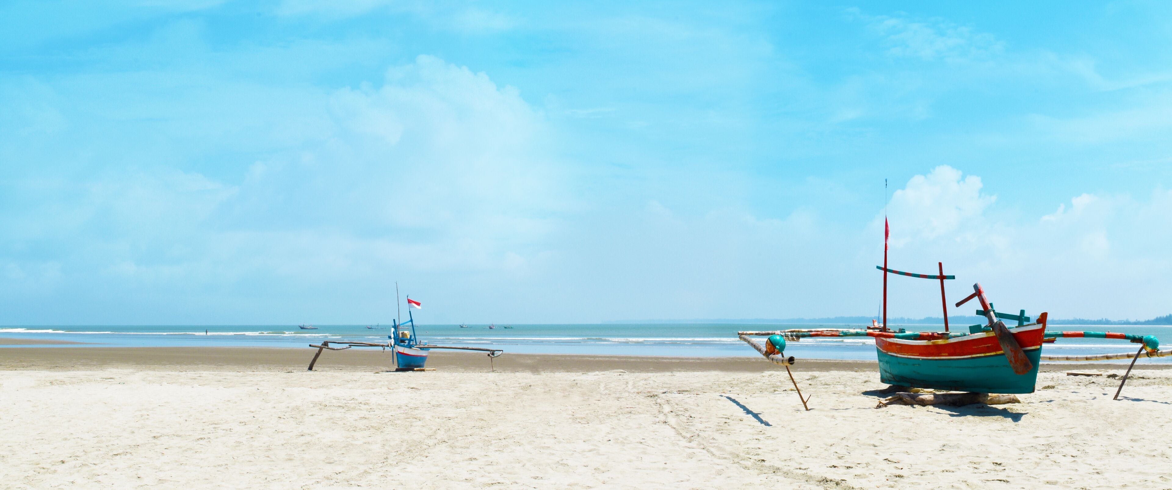 Panoramic beautiful tropical beach with wooden fishing boat and blue sky in the morning at Bengkulu beach Indonesia.
