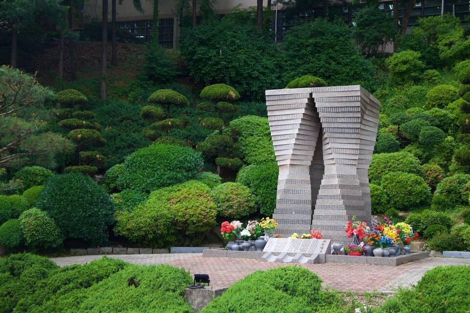 A stone monument with a unique stepped design surrounded by well-maintained bushes and flowers.