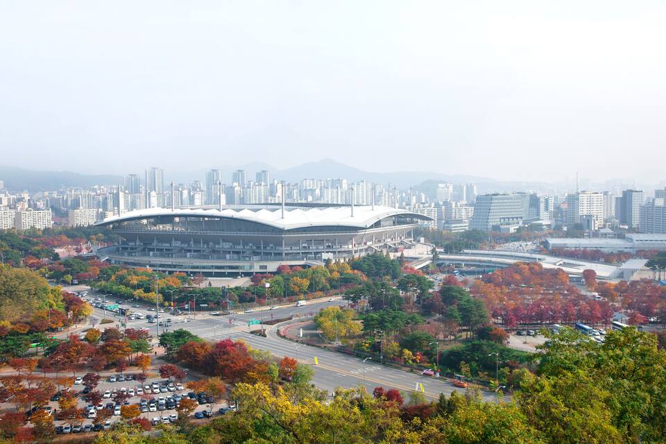 En stadsbild med höstlövsverk, en stor stadion och en tät stadsbild med många höga byggnader.