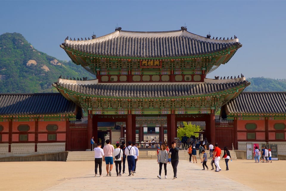 A traditional Korean gate with intricate designs and multiple levels, set against a backdrop of lush green mountains.
