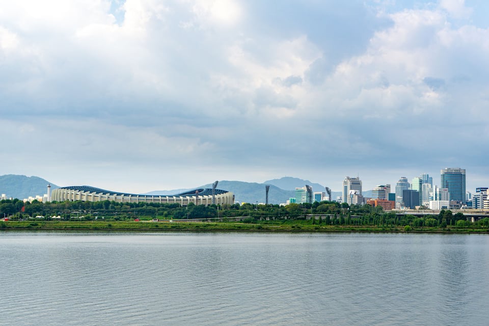 A city skyline with modern buildings and a large stadium by a body of water.