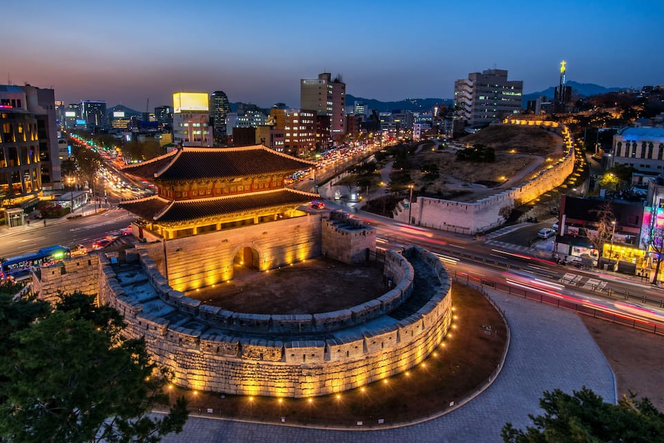 A historic walled city with illuminated buildings and a prominent traditional gate.